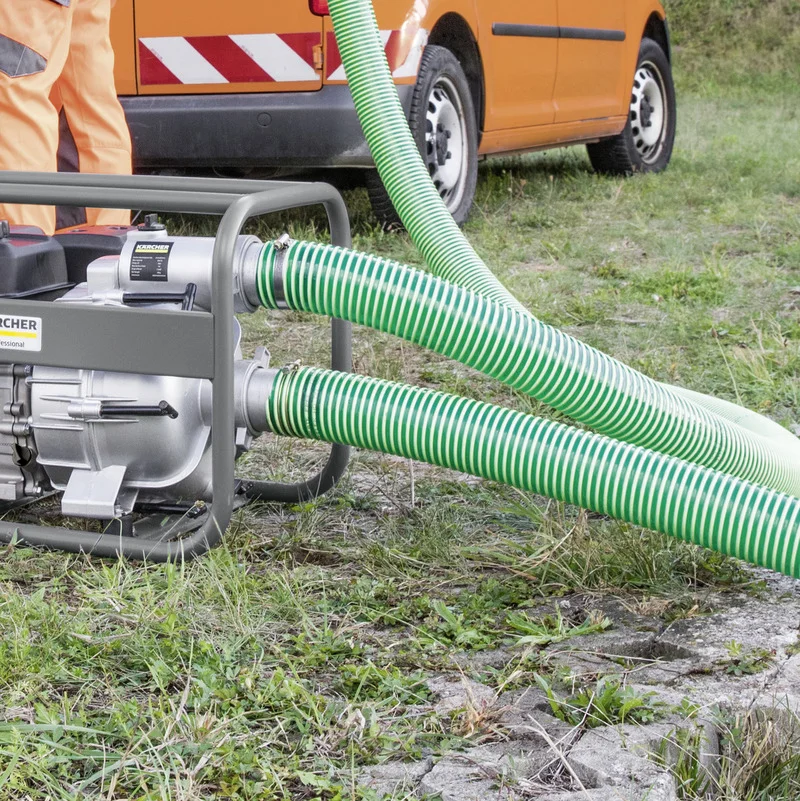Kärcher Wasserpumpe mit grünen Schläuchen im Freien, neben einem orangefarbenen Fahrzeug. Person in orangefarbener Arbeitskleidung.