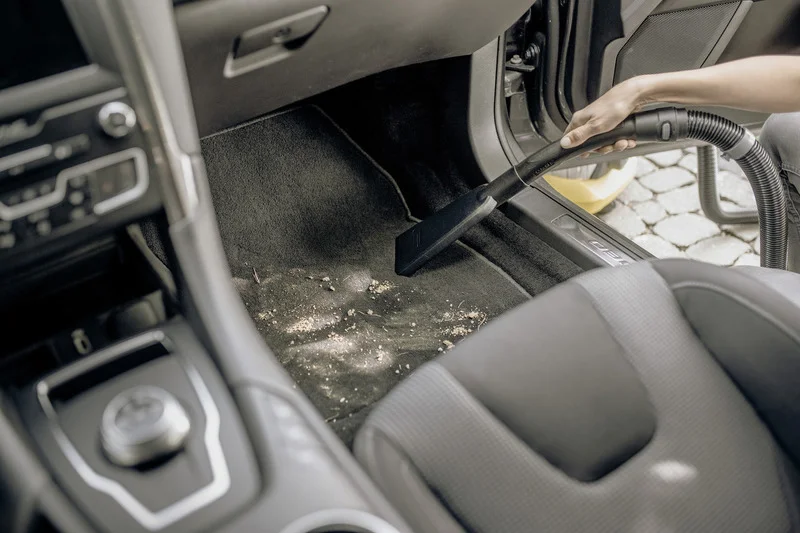 Person reinigt Autofußmatte mit Kärcher Staubsauger. Innenraum eines Autos, Staub und Schmutz auf dem Teppich.