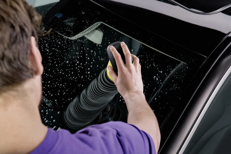 Person reinigt Autofenster mit Kärcher Fensterreiniger, Handbewegung sichtbar, Wasserflecken auf Glas.