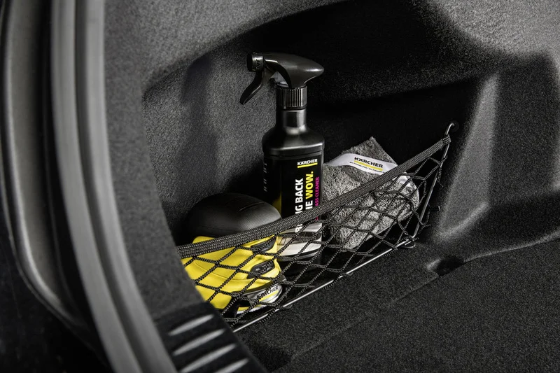 Kofferraum mit Kärcher Autopflegeprodukten: Sprühflasche, gelbes Gerät, graues Tuch in Netzhalterung.