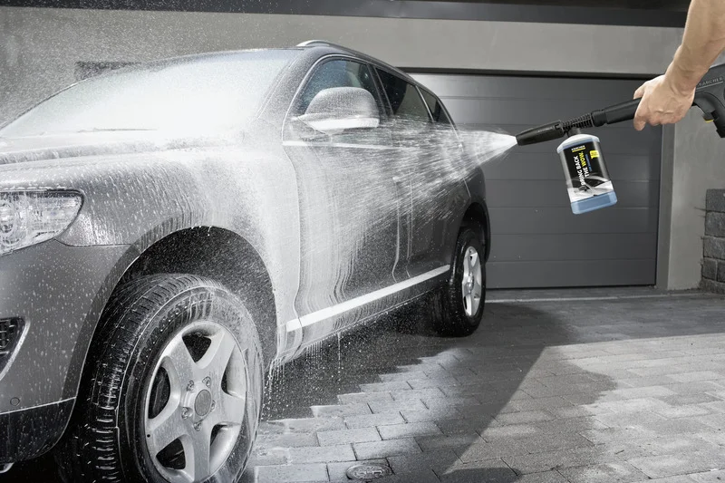 Auto wird mit Kärcher Hochdruckreiniger im Freien gewaschen, Wasserstrahl trifft auf die Karosserie.