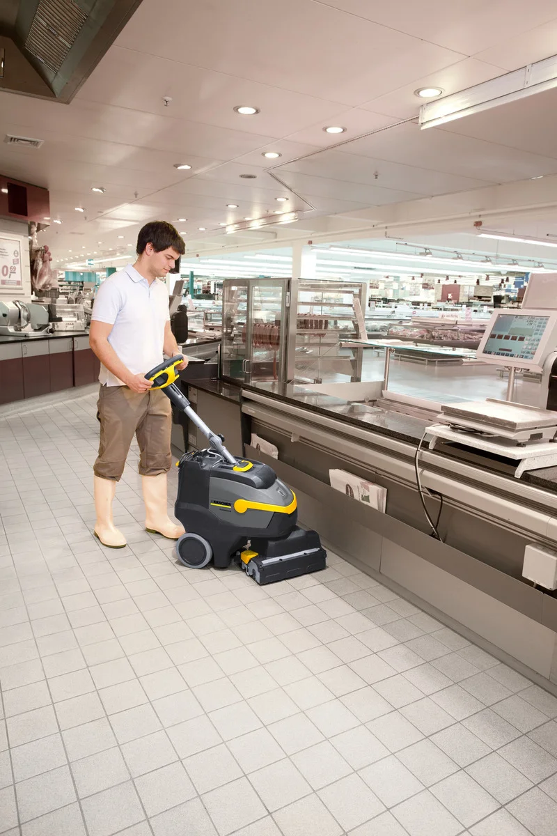 Mann bedient Kärcher Bodenreinigungsmaschine in einem Supermarkt, umgeben von Verkaufsregalen und Beleuchtung.