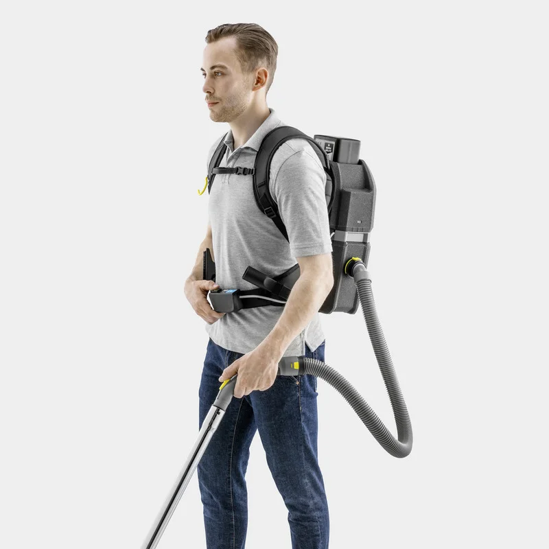 Person trägt einen Kärcher Rucksack-Staubsauger, graues T-Shirt, blaue Jeans, hält Staubsaugerrohr, weißer Hintergrund.