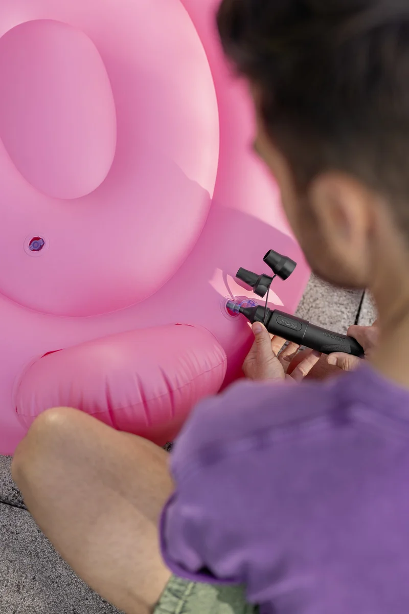 Mann pumpt rosa aufblasbares Kissen mit schwarzer Luftpumpe auf. Fokus auf Kissen und Pumpe, unscharfer Hintergrund.