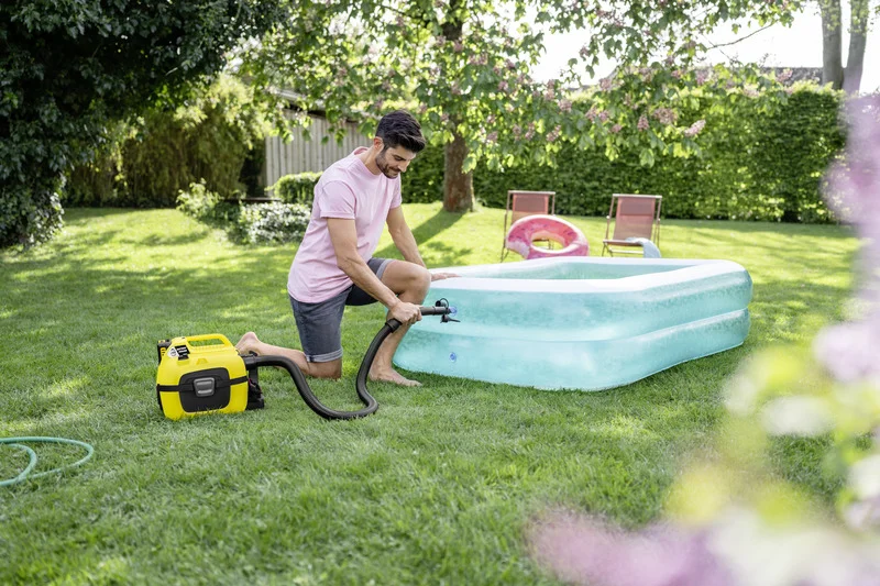 Mann füllt auf einer grünen Wiese ein aufblasbares Pool mit einem Kärcher Nass-Trockensauger. Im Hintergrund sind Gartenmöbel.
