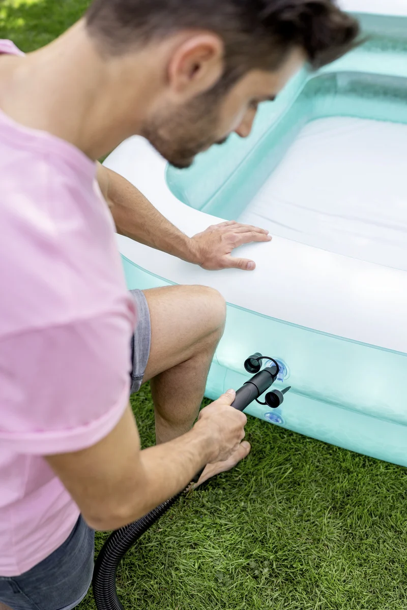 Person pumpt ein aufblasbares Schwimmbecken im Garten auf, trägt ein rosa T-Shirt und graue Shorts.
