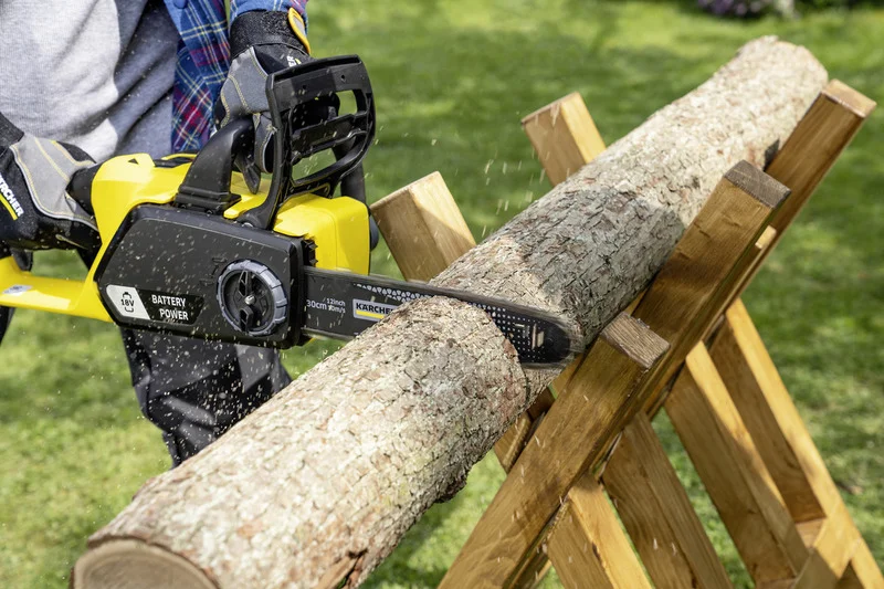 Person schneidet Holzstamm mit einer Kärcher Akku-Kettensäge im Freien auf einem Holzgestell.