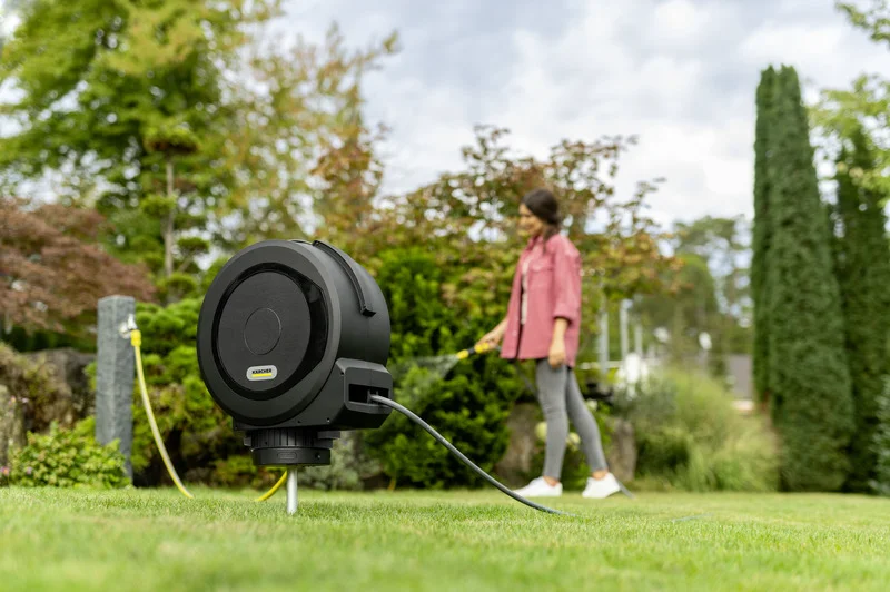 Kärcher Schlauchbox im Garten, im Hintergrund eine Person mit Gartenschlauch.