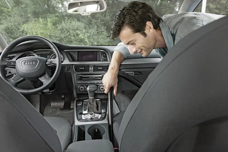 Innenraum eines Audi mit einem Mann, der den Bereich zwischen den Vordersitzen mit einem Staubsauger reinigt.
