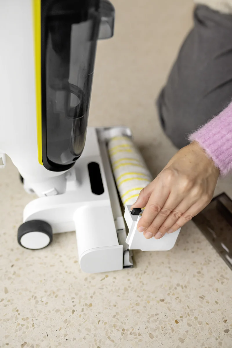Hand bedient Kärcher Bodenreiniger auf hellem Steinboden. Gerät hat gelbe Walze und schwarze Details.