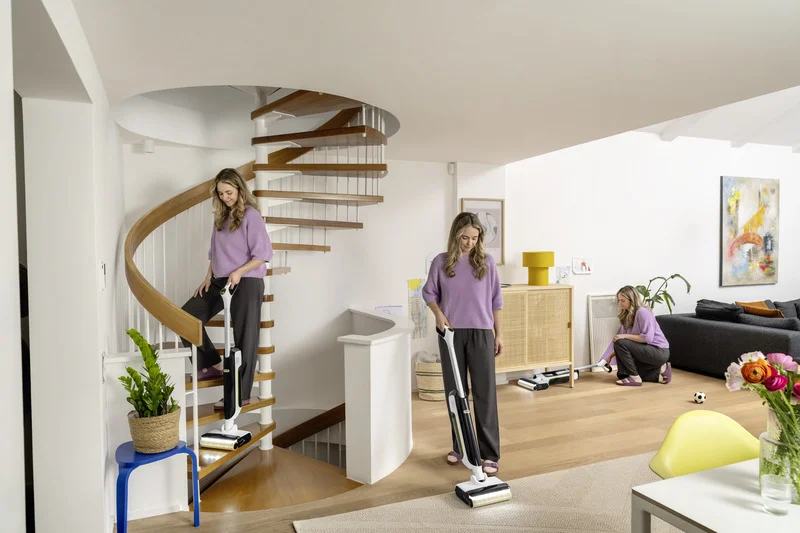 Frau reinigt in einem modernen Zuhause mit einem Kärcher Hartbodenreiniger eine Wendeltreppe und einen Holzboden. Sie wischt auch kniend den Boden.