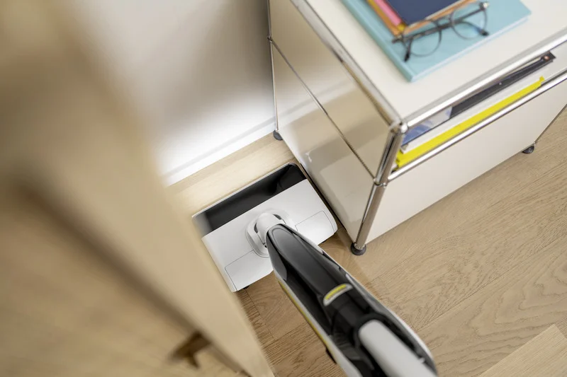 Kärcher Hartbodenreiniger reinigt einen hellen Holzfußboden unter einem modernen Schrank in einem Innenraum.