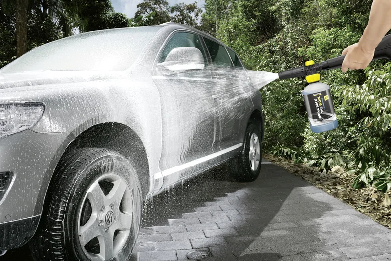 Auto wird mit Kärcher Hochdruckreiniger im Freien gewaschen, Wasserstrahl und Schaum auf der Karosserie.