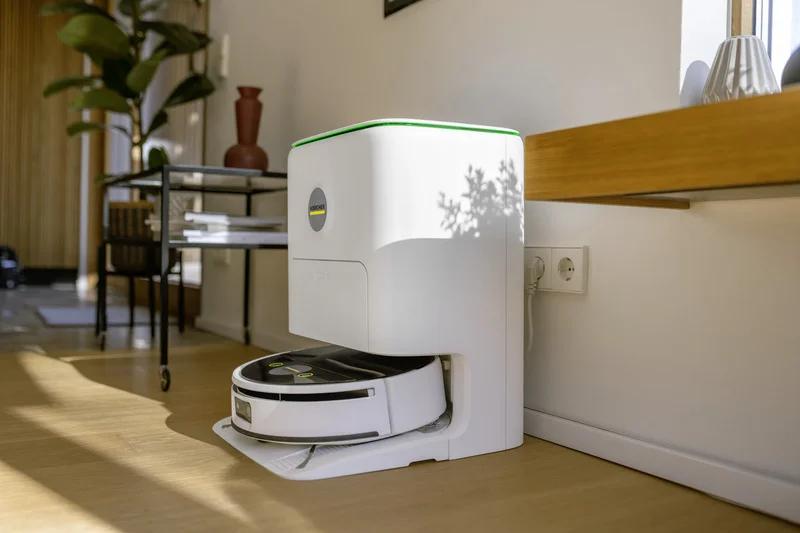 Ein weißer Kärcher Saugroboter in einer Ladestation in einem modernen Wohnzimmer mit Holzboden und Pflanzen.