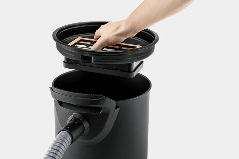 Hand legt Filter in Kärcher Aschesauger ein. Schwarzer Behälter mit Schlauchanschluss sichtbar.