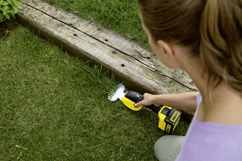 Person verwendet Kärcher Grasschere, um Gras entlang eines Holzbretts im Garten zu schneiden.