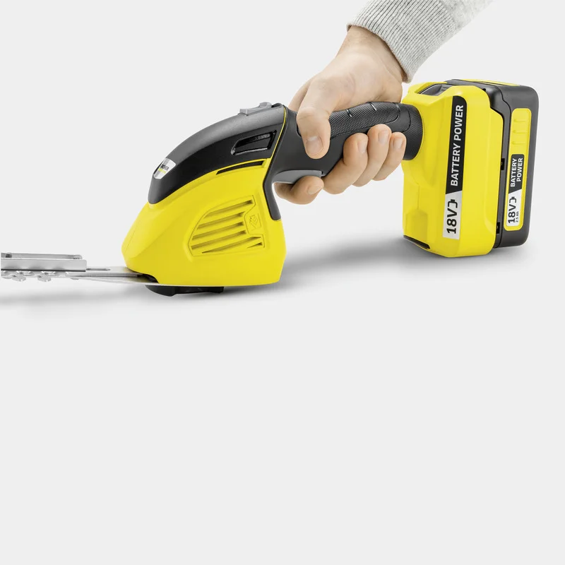 Hand hält einen gelben Kärcher Akku-Grasschneider mit 18V Batterie, vor weißem Hintergrund.