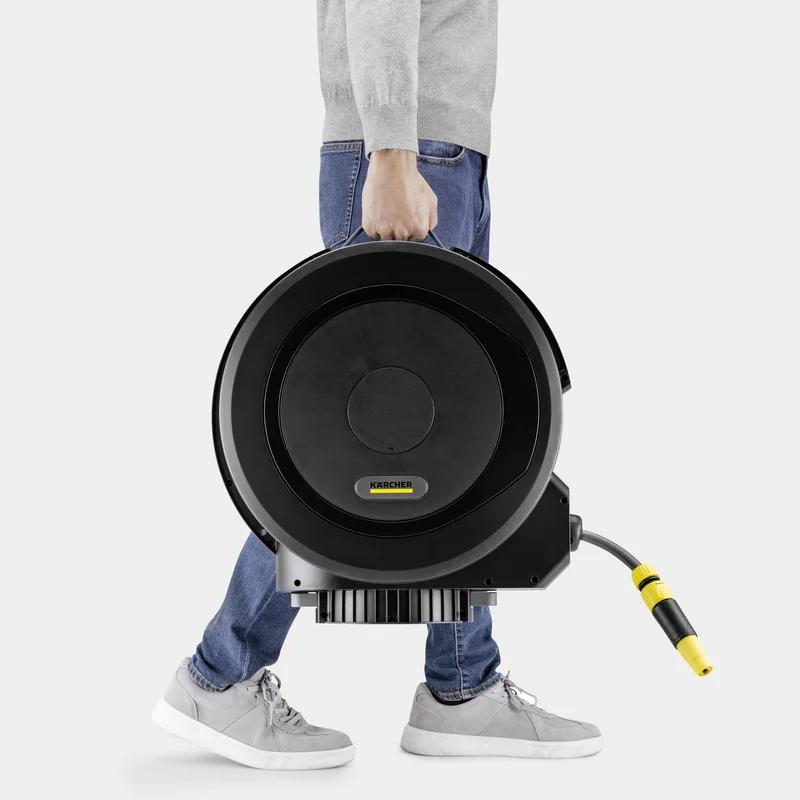 Person in Jeans und grauen Schuhen trägt eine Kärcher Schlauchtrommel.