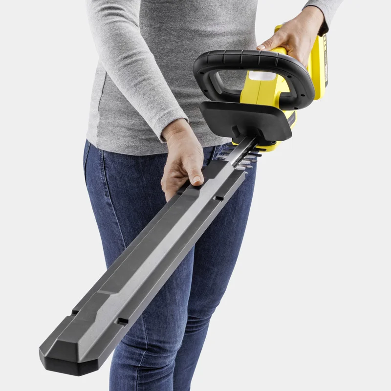 Person hält einen gelben Kärcher Heckenschneider, trägt graues Oberteil und blaue Jeans.