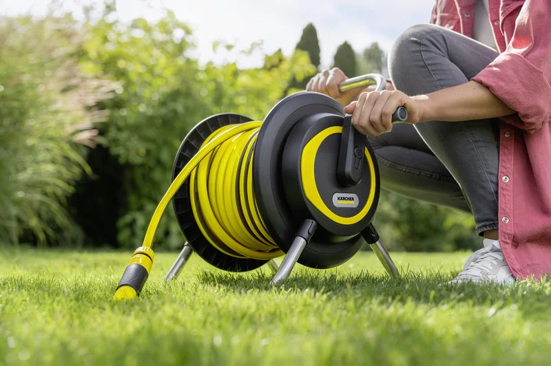 Person wickelt einen gelben Gartenschlauch auf eine Kärcher Schlauchtrommel im Garten.
