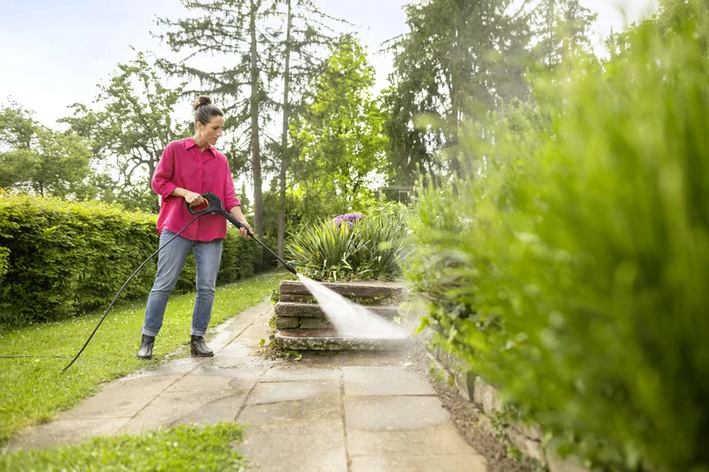 Person reinigt mit Kärcher Hochdruckreiniger eine Steintreppe im Garten. Umgeben von grünen Pflanzen und Bäumen.