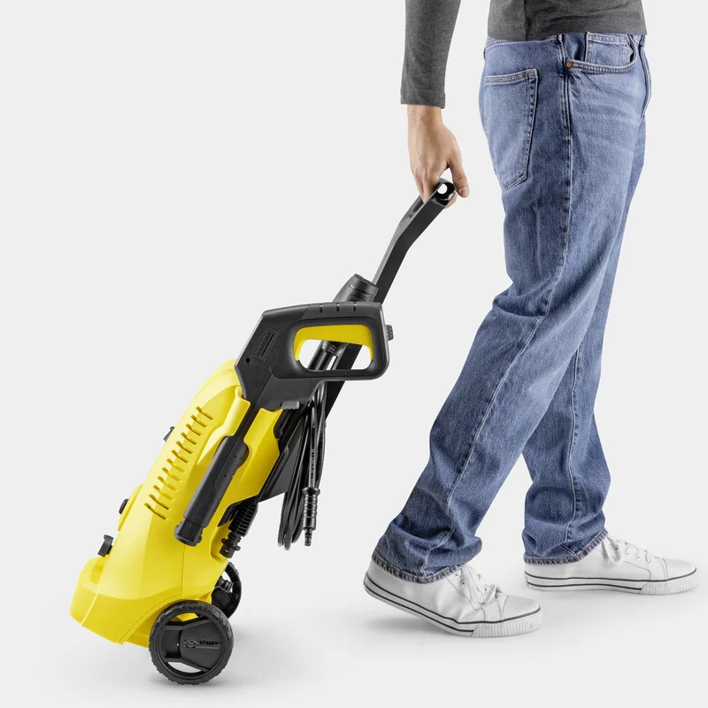 Person in Jeans und Sneakers zieht einen gelben Kärcher Hochdruckreiniger auf Rädern über einen hellen Boden.