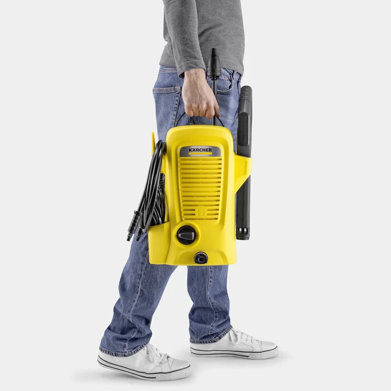 Person trägt einen gelben Kärcher Hochdruckreiniger in der Hand, während er Jeans und weiße Turnschuhe trägt.