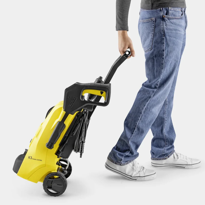 Person in Jeans zieht einen gelben Kärcher Hochdruckreiniger auf Rädern über einen hellen Boden.