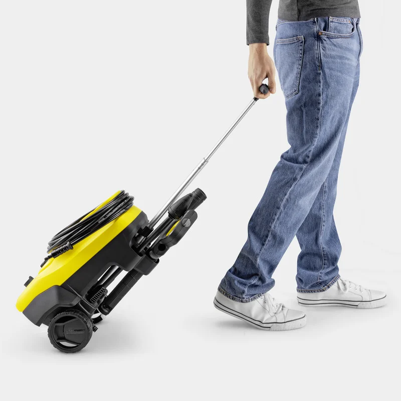 Person zieht einen gelben Kärcher Hochdruckreiniger auf Rädern, trägt blaue Jeans und weiße Turnschuhe.