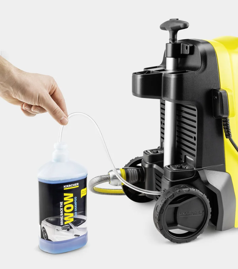 Hand hält Schlauch, der in eine Flasche mit Kärcher Autoshampoo führt, neben einem Kärcher Hochdruckreiniger.