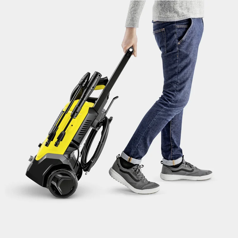 Person zieht einen gelben Kärcher Hochdruckreiniger auf Rollen, trägt Jeans und graue Schuhe.