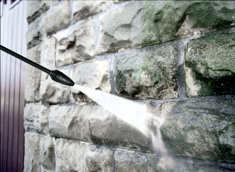 Kärcher Hochdruckreiniger sprüht Wasserstrahl auf eine mit Moos bedeckte Steinwand.
