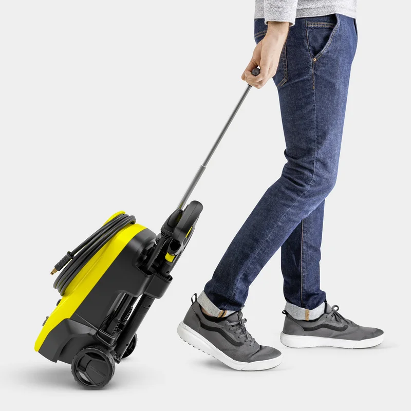 Person zieht einen gelben Kärcher Hochdruckreiniger auf Rollen, trägt Jeans und graue Sneakers.