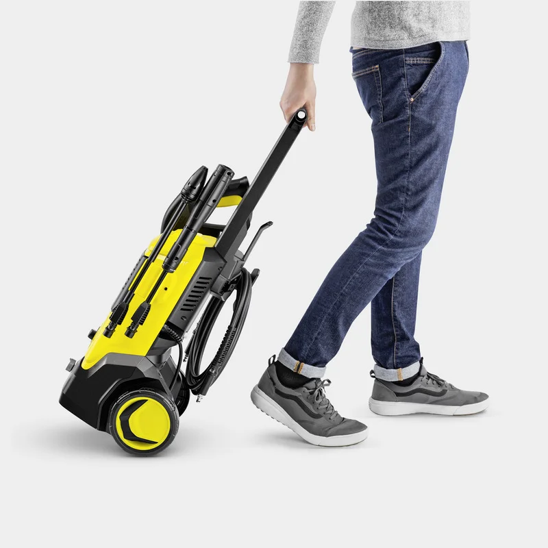 Person zieht einen gelben Kärcher Hochdruckreiniger auf Rollen, trägt Jeans und graue Schuhe.