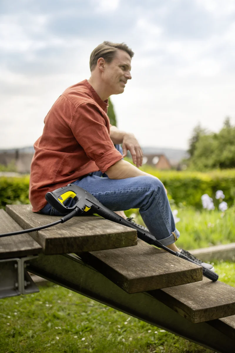 Mann in rotem Hemd und Jeans sitzt auf Holztreppe im Garten, neben ihm ein Kärcher Hochdruckreiniger.