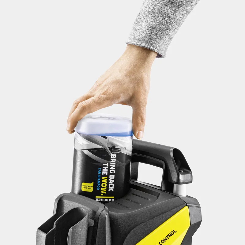 Hand platziert Kärcher Autoshampoo auf einem Kärcher Hochdruckreiniger. Grauer Hintergrund, Nahaufnahme.