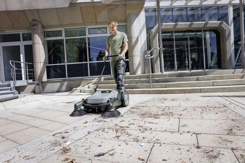Mann reinigt Außenbereich mit Kärcher Kehrmaschine, umgeben von modernen Gebäuden und Treppen.