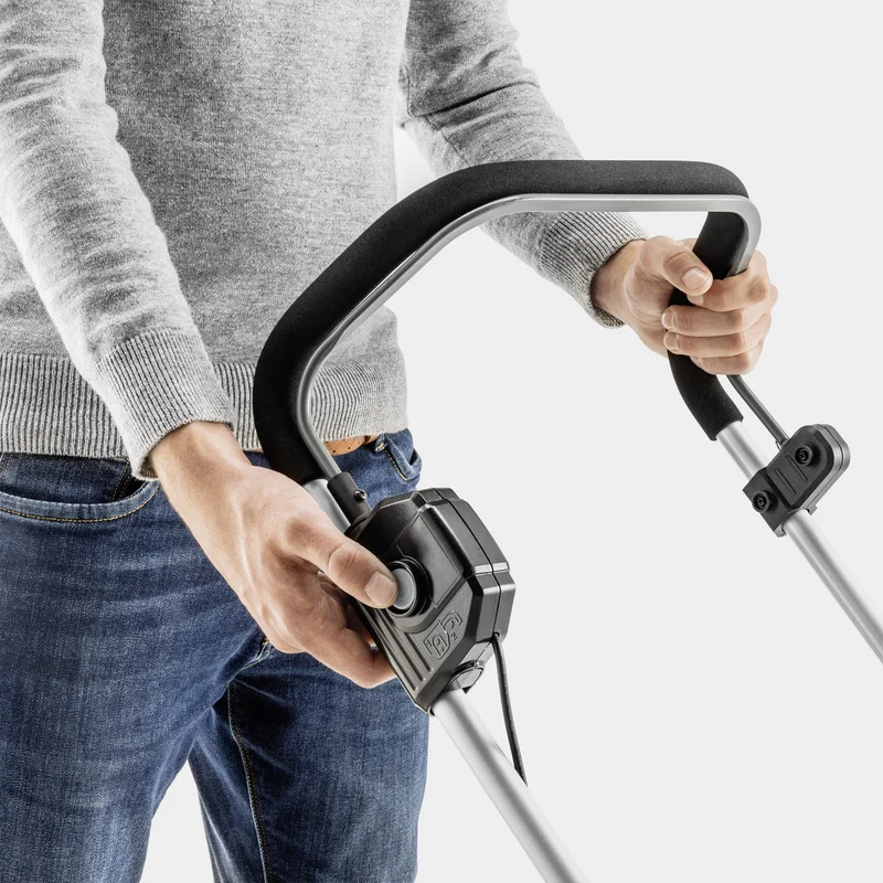 Person in grauem Pullover und Jeans hält den Griff eines Kärcher Geräts mit Steuerungsknopf.