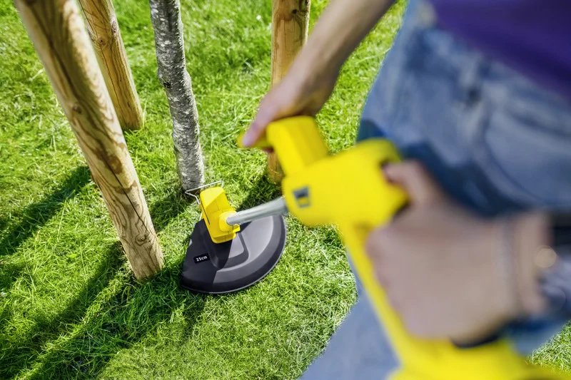 Person reinigt Gras um Baum mit Kärcher Rasentrimmer.
