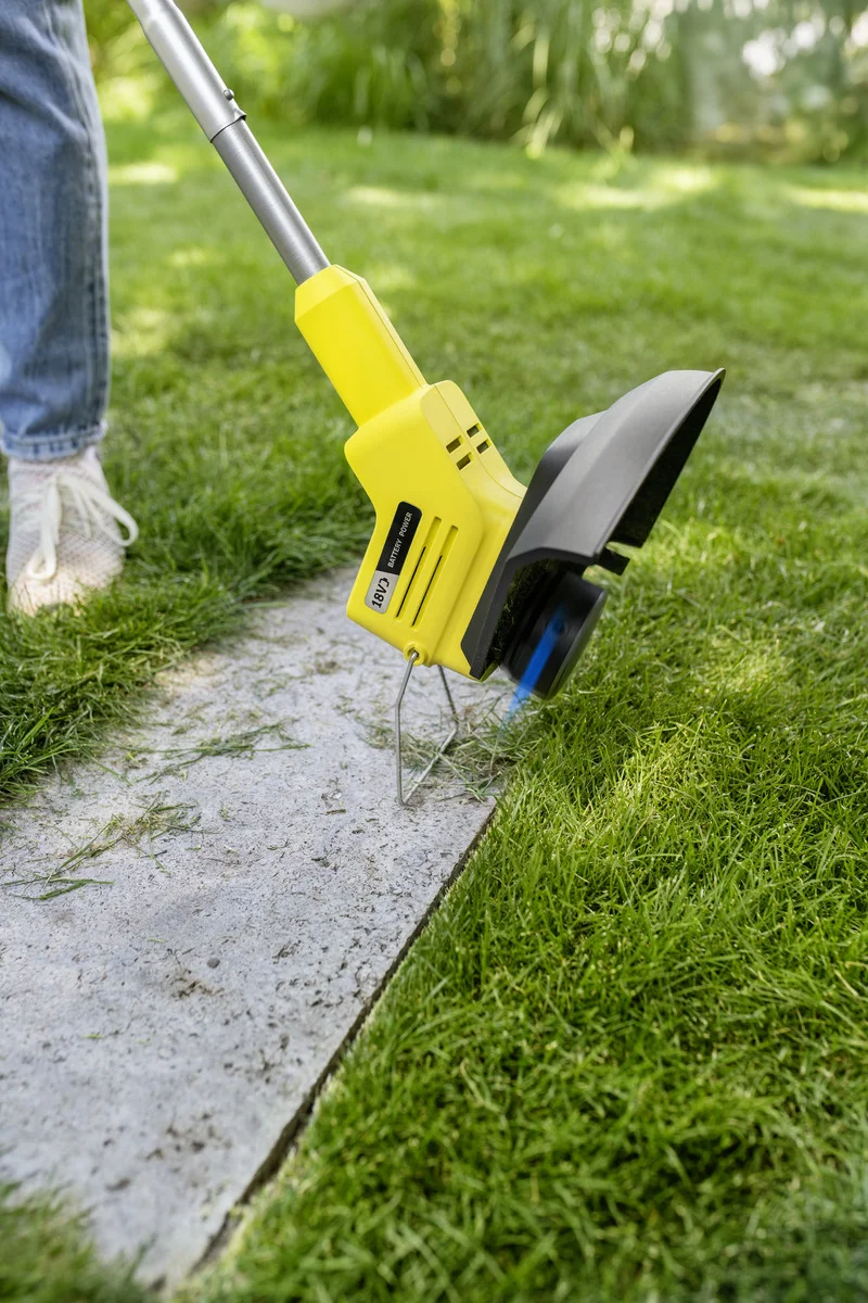Person nutzt Kärcher Rasenkantenschneider auf einem Gartenweg. Der Rasenkantenschneider schneidet Gras entlang einer Steinplatte.