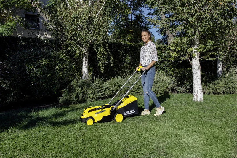 Person mäht Rasen mit einem Kärcher Rasenmäher in einem Garten, umgeben von Bäumen und Sträuchern.
