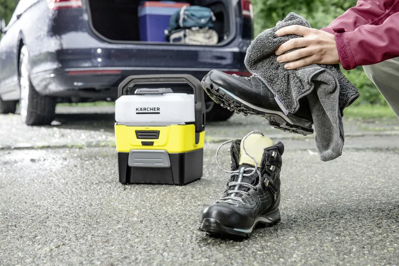 Person reinigt Wanderschuh mit Kärcher Outdoor Cleaner, Auto im Hintergrund.