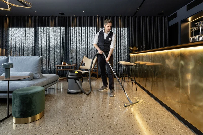 Person reinigt Boden mit Kärcher Nass-/Trockensauger in modernem Wohnzimmer mit Sofa, Hocker und goldener Bar.