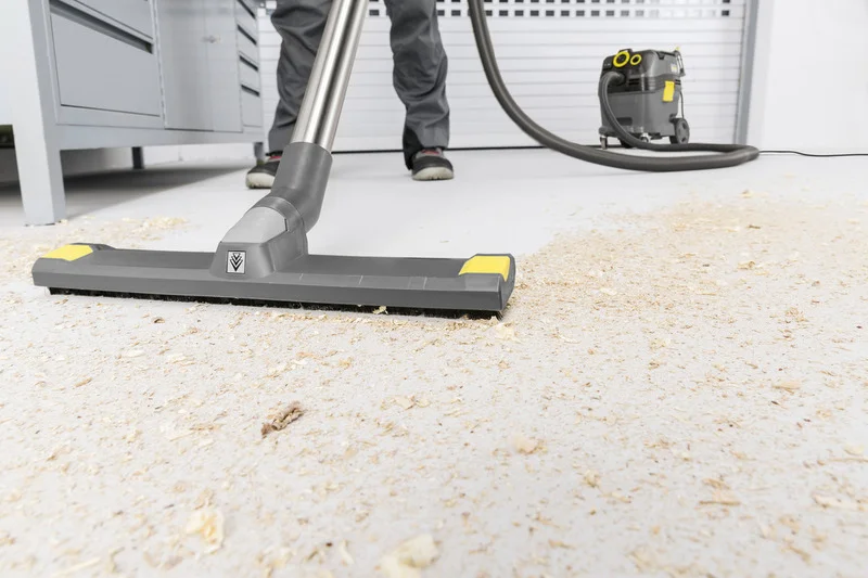 Kärcher Industriesauger saugt Holzspäne auf Werkstattboden, Person im Hintergrund, grauer Boden und Schränke.