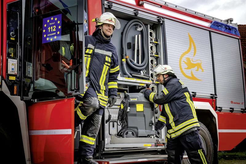 Feuerwehrleute in Schutzkleidung entladen einen Kärcher Nass-/Trockensauger aus einem Feuerwehrfahrzeug.