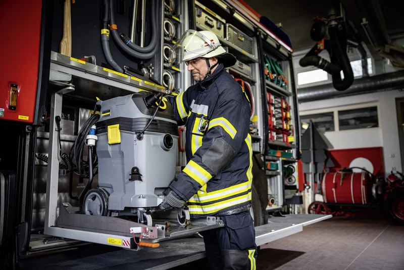 Feuerwehrmann in Schutzkleidung entnimmt einen Kärcher Nass-/Trockensauger aus einem Feuerwehrauto in einer Garage.