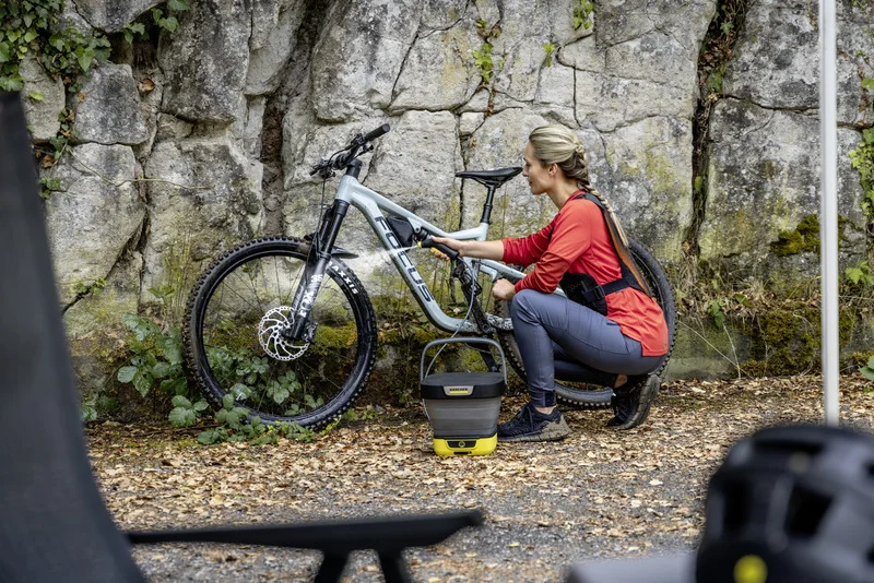 Frau reinigt ein Focus-Mountainbike mit einem Kärcher tragbaren Reiniger vor einer Felswand im Freien.