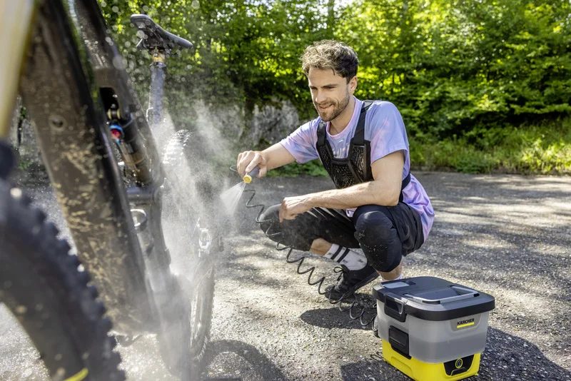 Person reinigt Fahrrad mit Kärcher mobiler Reiniger im Freien. Fahrrad wird mit Wasserstrahl abgespritzt.