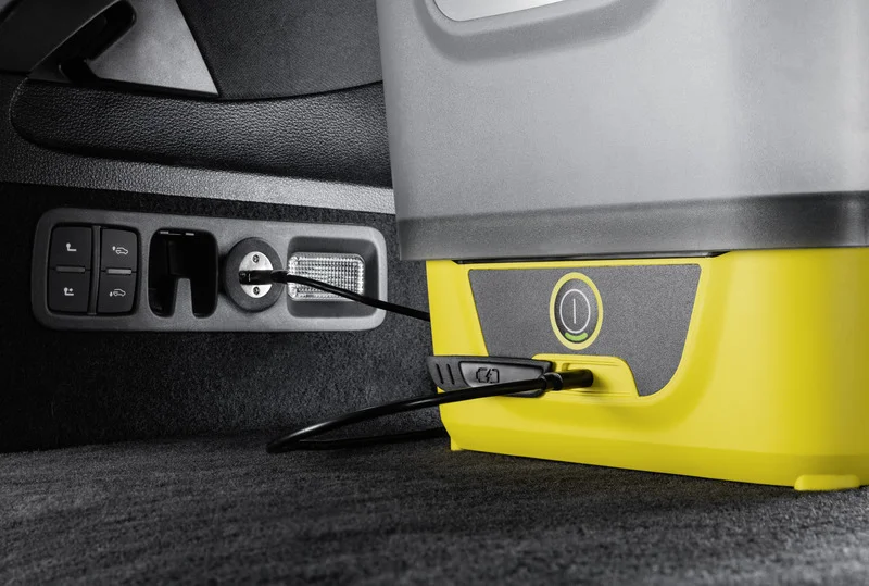Kärcher Gerät im Auto angeschlossen, mit Kabel verbunden. Schwarze Knöpfe und Steckdose im Hintergrund.