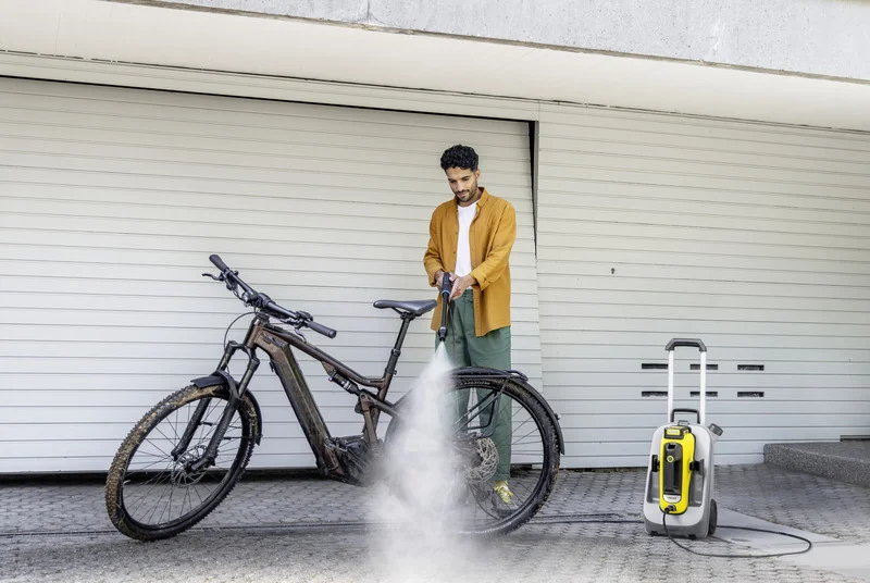 Person reinigt ein Fahrrad mit einem Kärcher Hochdruckreiniger vor einer geschlossenen Garagentür.